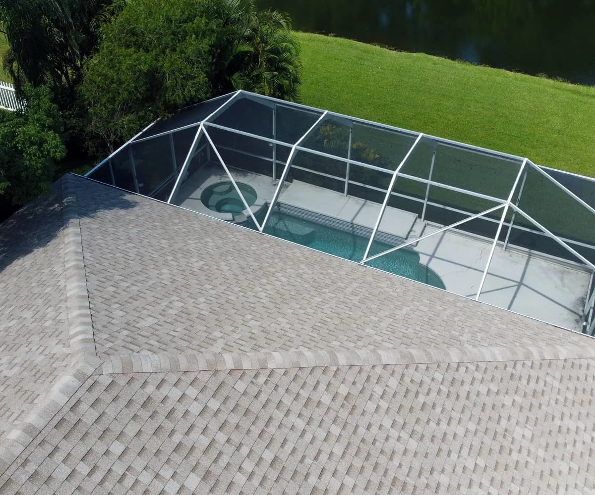 Aerial view of a shingle roof and screened pool by a lake