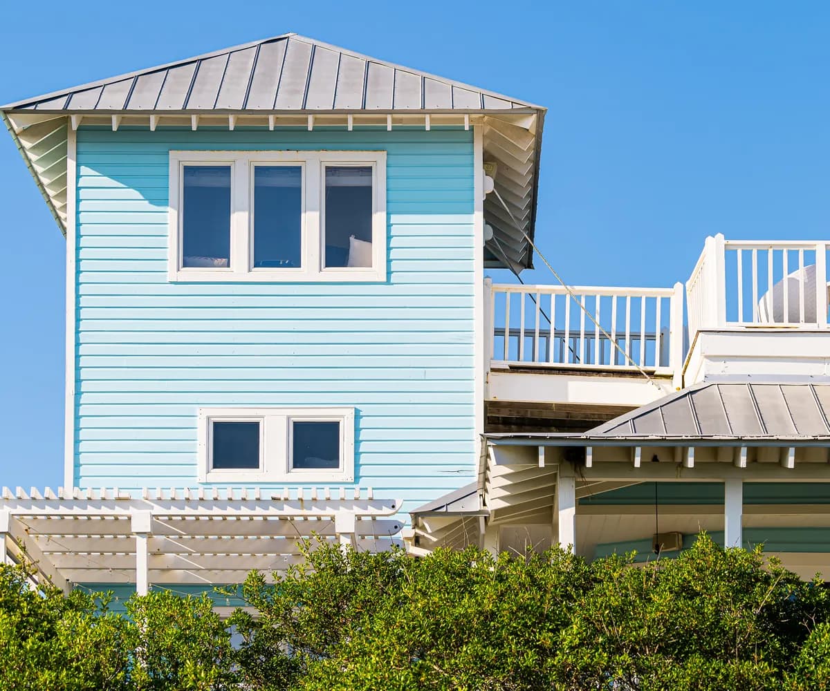 Pastel blue beach house with standing seam metal roofs and a rooftop deck