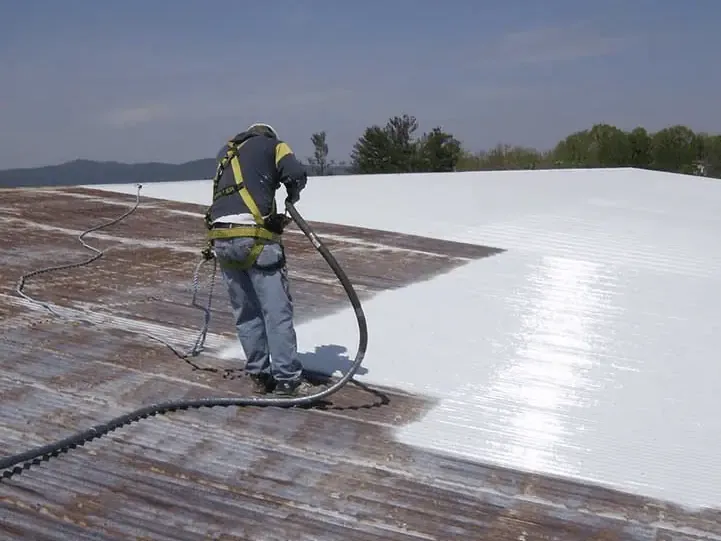 Roofer spraying a white coating on a metal roof