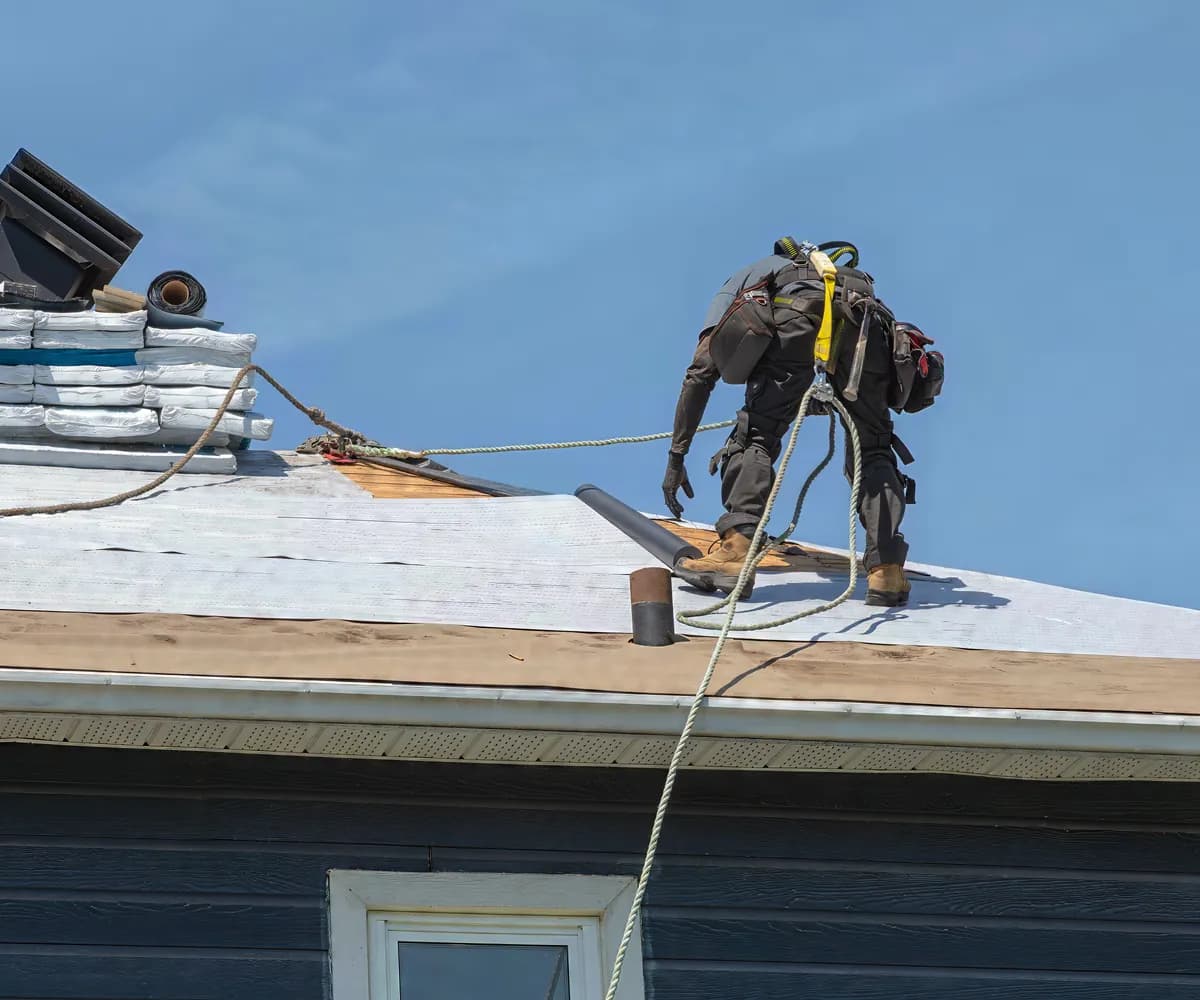 Roofer in a safety harness laying underlayment
