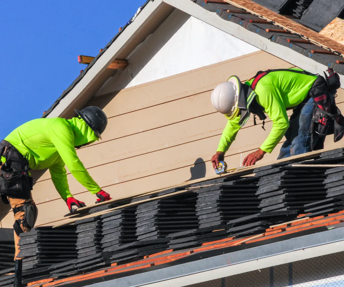 Two roofers in safety gear installing a tile roof