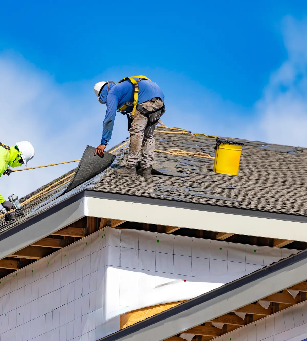 Roofers installing underlayment and shingles on a new roof
