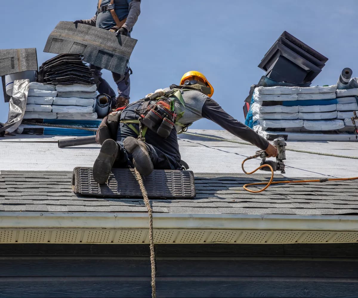 Roofing crew in harnesses and hard hats installing shingles