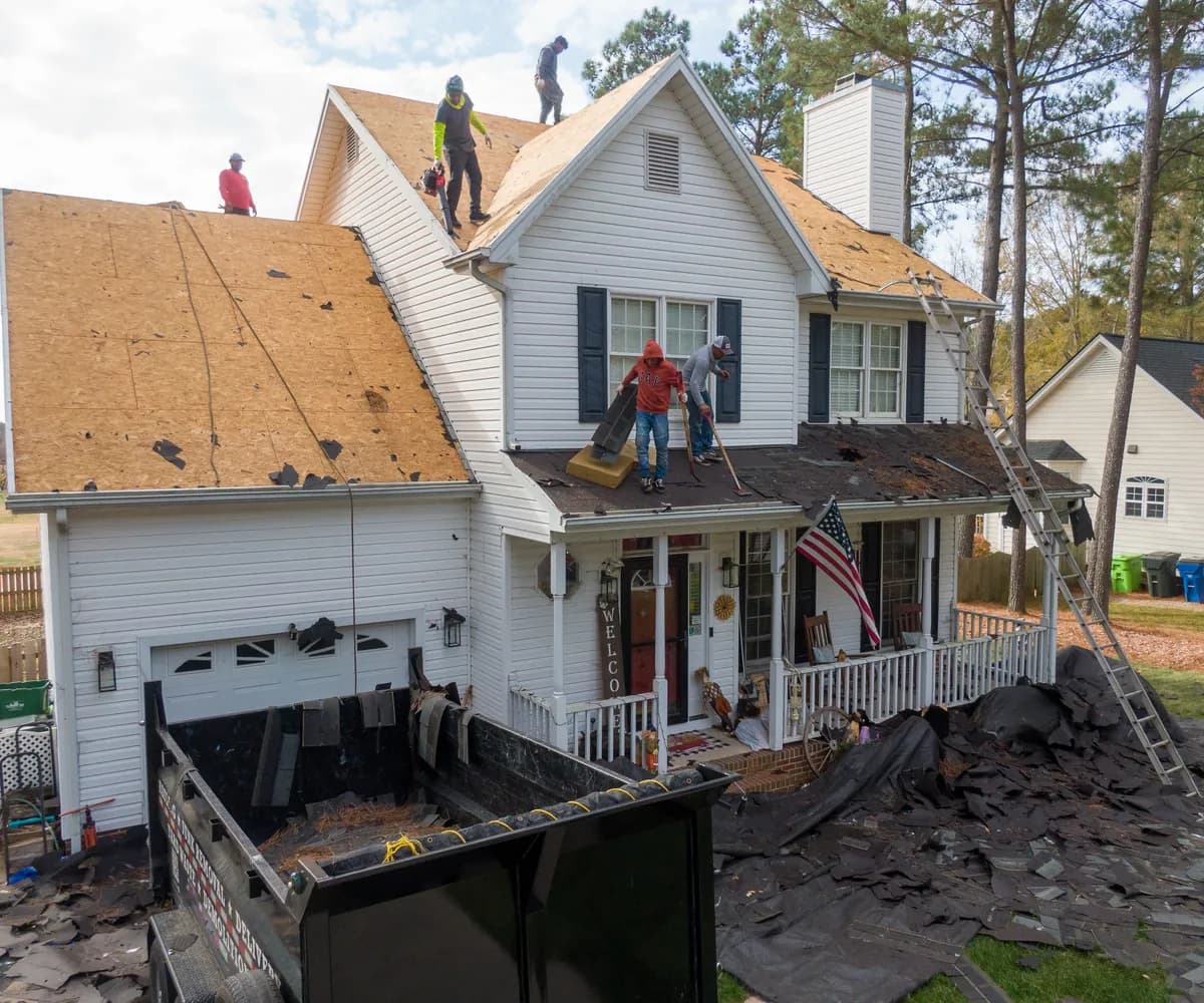 Roofing crew tearing off an old roof, with a dumpster in the driveway